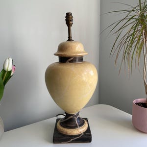 May include: A ceramic table lamp with a yellow and brown marbled design. The lamp has a round base and a square base.