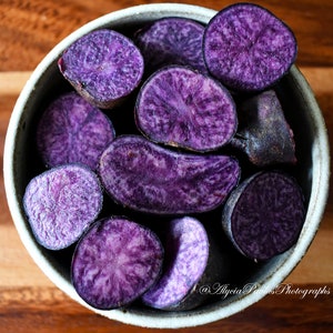 May include: A bowl filled with purple potatoes, sliced in half and arranged in a circular pattern. The potatoes have a vibrant purple hue and a slightly textured surface.