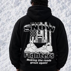 May include: A black hooded sweatshirt featuring a graphic on the back with a snowplow, a stylized American flag, and the text SNOW FIGHTERS Making the roads great again! The hoodie is worn with a black knit beanie and dark brown pants.