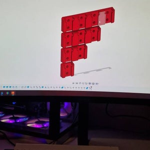Puede incluir: Un monitor de ordenador muestra un modelo 3D de un componente modular rojo. El dise&ntilde;o est&aacute; dispuesto en una configuraci&oacute;n vertical escalonada. Un teclado blanco est&aacute; en primer plano.