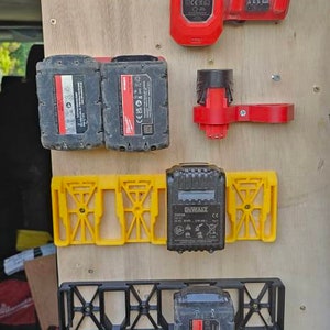 Puede incluir: Una colecci&oacute;n de accesorios para herramientas el&eacute;ctricas, que incluye soportes de bater&iacute;a rojos y amarillos, un cargador r&aacute;pido rojo y bater&iacute;as negras. Los art&iacute;culos est&aacute;n montados sobre una superficie de madera.