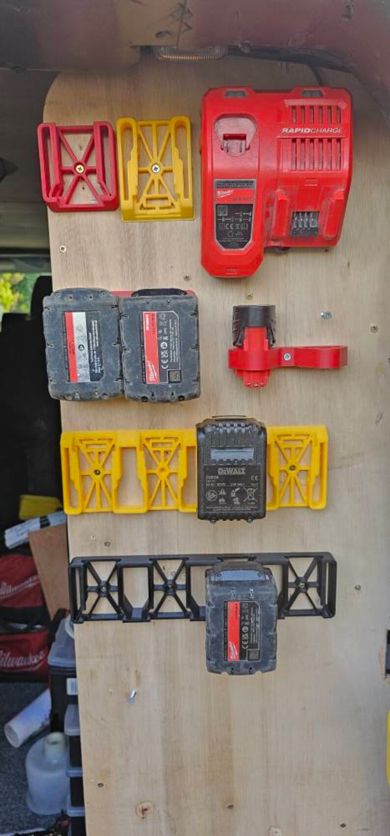 Puede incluir: Una colecci&oacute;n de accesorios para herramientas el&eacute;ctricas, que incluye soportes de bater&iacute;a rojos y amarillos, un cargador r&aacute;pido rojo y bater&iacute;as negras. Los art&iacute;culos est&aacute;n montados sobre una superficie de madera.