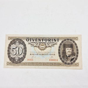 May include: A vintage Hungarian 50 Forint banknote featuring a portrait of a man in a fur hat and a large "50" in the center. The text "ÖTVEN FORINT" is printed at the top of the note, and the text "MAGYAR NEMZETI BANK" is printed in the center.
