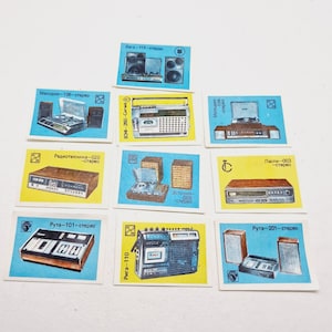 May include: A collection of nine vintage matchbox labels featuring illustrations of different stereo systems. The labels are blue and yellow with white text. The text on the labels includes the names of the stereo systems, such as "Melodia-106-stereo", "Radiotehnika-020", and "Ruta-101-stereo".