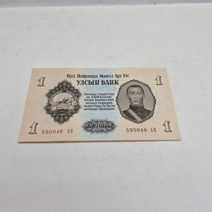 May include: A one Mongolian tugrik banknote featuring a portrait of a man in a suit and a seal with the text "БНМАУ" in Cyrillic script. The text "Бүгд Найрамдах Монгол Ард Улс" and "УЛСЫН БАНК" are printed in Cyrillic script. The banknote also features the text "НЭГ ТӨГРӨГ" and the year "1955".