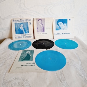 Könnte beinhalten: Vier Vintage-Schallplatten mit blauen und schwarzen Etiketten. Die Schallplatten liegen auf einer weißen Oberfläche mit drei Schallplattenhüllen. Die Hüllen zeigen Schwarzweißfotos von Sängern und den Text "Вадим Мулерман", "Юрий Горобец", "Галина Ненашева", und "Николай Никитский".