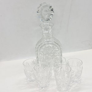 Puede incluir: Un juego de seis vasos de chupito de vidrio transparente y una jarra de vidrio transparente con un tapón decorativo. Los vasos y la jarra tienen un diseño de vidrio cortado.