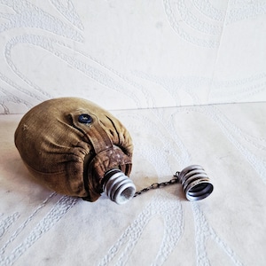 May include: A vintage olive drab canvas canteen with a metal cap and chain. The canteen has a brown leather strap and a button closure. The metal cap is silver with a ribbed design. The canteen is likely from the military.