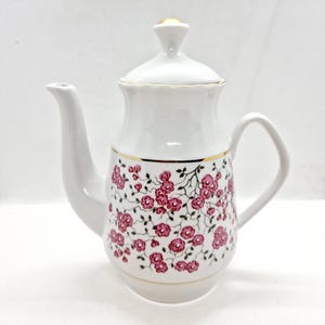 May include: White porcelain teapot with a gold trim and a pink floral pattern. The teapot has a lid and a handle.