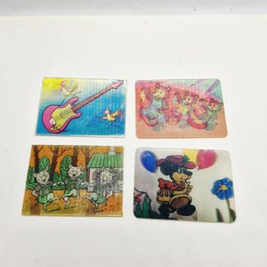 May include: Four vintage, rectangular plastic cards with colorful cartoon illustrations. One card features a pink guitar, another dancing bears, a third dancing pigs, and the last a mouse with balloons.