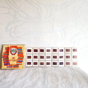May include: A collection of vintage slides and a booklet featuring Soviet Union imagery. The booklet has a red, gold, and blue design with the text "СОЮЗ НЕРУШИМЫЙ". The slides are in white frames, displaying various images.