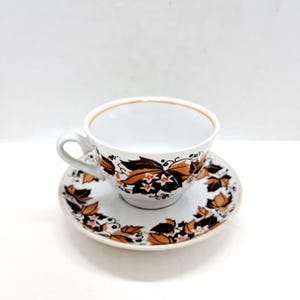 May include: A white porcelain teacup and saucer set with a brown and orange floral pattern. The cup has a rounded shape and a handle. The saucer has a matching floral pattern.