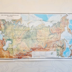 May include: A vintage map of the Soviet Union, titled "Soyuz Sovetskikh Sotsialisticheskikh Respublik" (Union of Soviet Socialist Republics). The map is printed in black, brown, blue, and green, and shows the major geographical features of the country.
