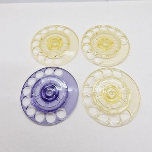 Può includere: Quattro bobine di plastica, due gialle e due viola, con fori circolari attorno al bordo. Le bobine sono progettate per contenere filo o lana.