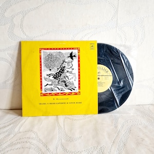 May include: A vintage vinyl record album with a yellow cover featuring a black and white illustration of a fairytale scene. The album is partially visible, with the record inside a plastic sleeve.