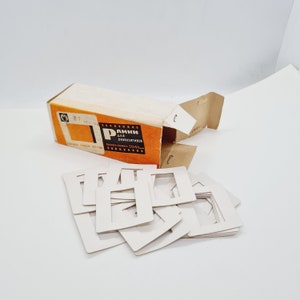 May include: A box of white cardboard frames for 50x50mm slides. The box is open and the frames are scattered on a white surface. The box is labeled "РАМКИ ДЛЯ ДИАПОЗИТИВОВ РАЗМЕР РАМКИ 50x50мм"