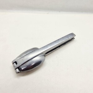 May include: A silver-colored nutcracker with a hinged design. The nutcracker has a rounded, bulbous shape at one end and a long, flat handle. The tool is made of metal and appears to be vintage.