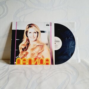May include: A vintage vinyl record album cover featuring a woman with long blonde hair. The album is titled "Poet Dalida" and the record label is "Ariola".