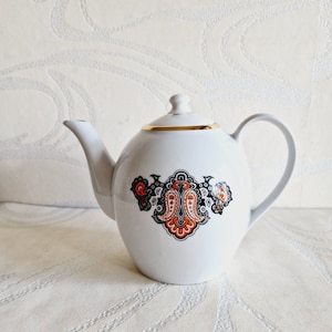 May include: White teapot with a gold rim and a black, orange, and white paisley design.