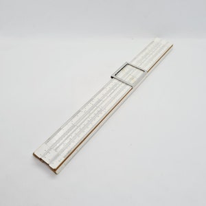 May include: A vintage silver slide rule with a wooden base and a metal slider. The slide rule is a tool used for mathematical calculations.
