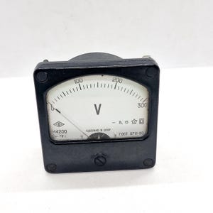 May include: A black analog voltmeter with a white face and a needle indicating a voltage reading. The face displays the letter "V" and numbers up to 300. The text "MADE IN USSR" is visible.