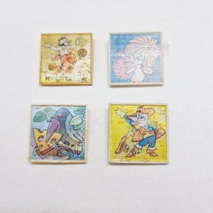 May include: Four vintage square-shaped pins with colorful illustrations. The pins feature a man juggling balls, a girl with a large ball, a crow with a piece of cheese, and a cat dressed as a scarecrow.
