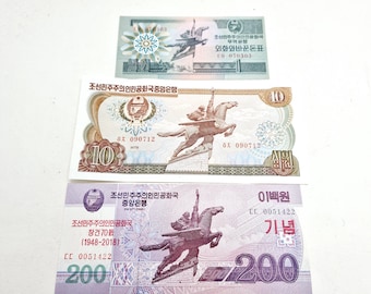 May include: Three North Korean banknotes are displayed, featuring images of a winged horse and rider. The bills are in various denominations, with text in Korean. The top bill is light green, the middle is tan, and the bottom is purple.