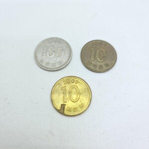 May include: Three South Korean coins: a silver-colored 100 won coin dated 1992, a bronze-colored 10 won coin dated 1987, and a brass-colored 10 won coin dated 2003. Each coin features its denomination in large numerals and Korean text.