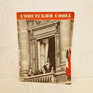 May include: A vintage magazine cover featuring the text "Soviet Union" in red letters, with a black and white photo of a group of men standing on a balcony, waving to a crowd. The magazine is dated 1940.