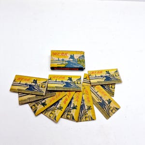 Puede incluir: Una caja de 10 cuchillas de afeitar vintage con un diseño amarillo y azul. La caja está etiquetada "HEBA" y presenta una imagen de un carruaje tirado por caballos.