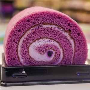 Peut inclure: Un g&acirc;teau roul&eacute; violet et blanc dans un r&eacute;cipient en plastique noir.