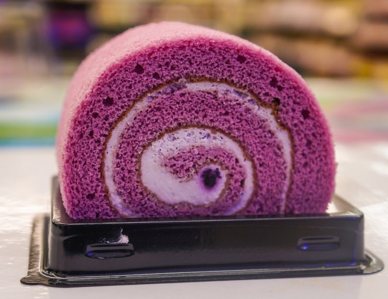 Peut inclure: Un g&acirc;teau roul&eacute; violet et blanc dans un r&eacute;cipient en plastique noir.