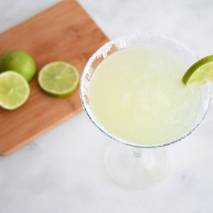 a glass of margarita with slices of key lime