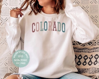 May include: A white sweatshirt with the word "COLORADO" printed in rainbow colors. The sweatshirt has a tag that says "Water Based Inks, Eco, Non-Toxic, PVC Free".