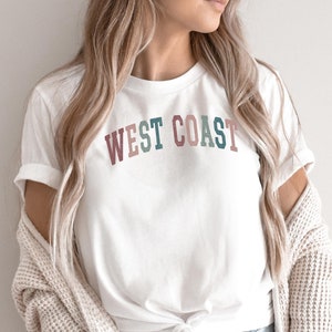May include: A white t-shirt with the text "WEST COAST" in colorful letters. The letters are in shades of pink, green, and blue.