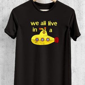 May include: Black t-shirt with a yellow submarine graphic and the text "we all live in a". The submarine has red and orange accents. The shirt is hanging on a wooden hanger.