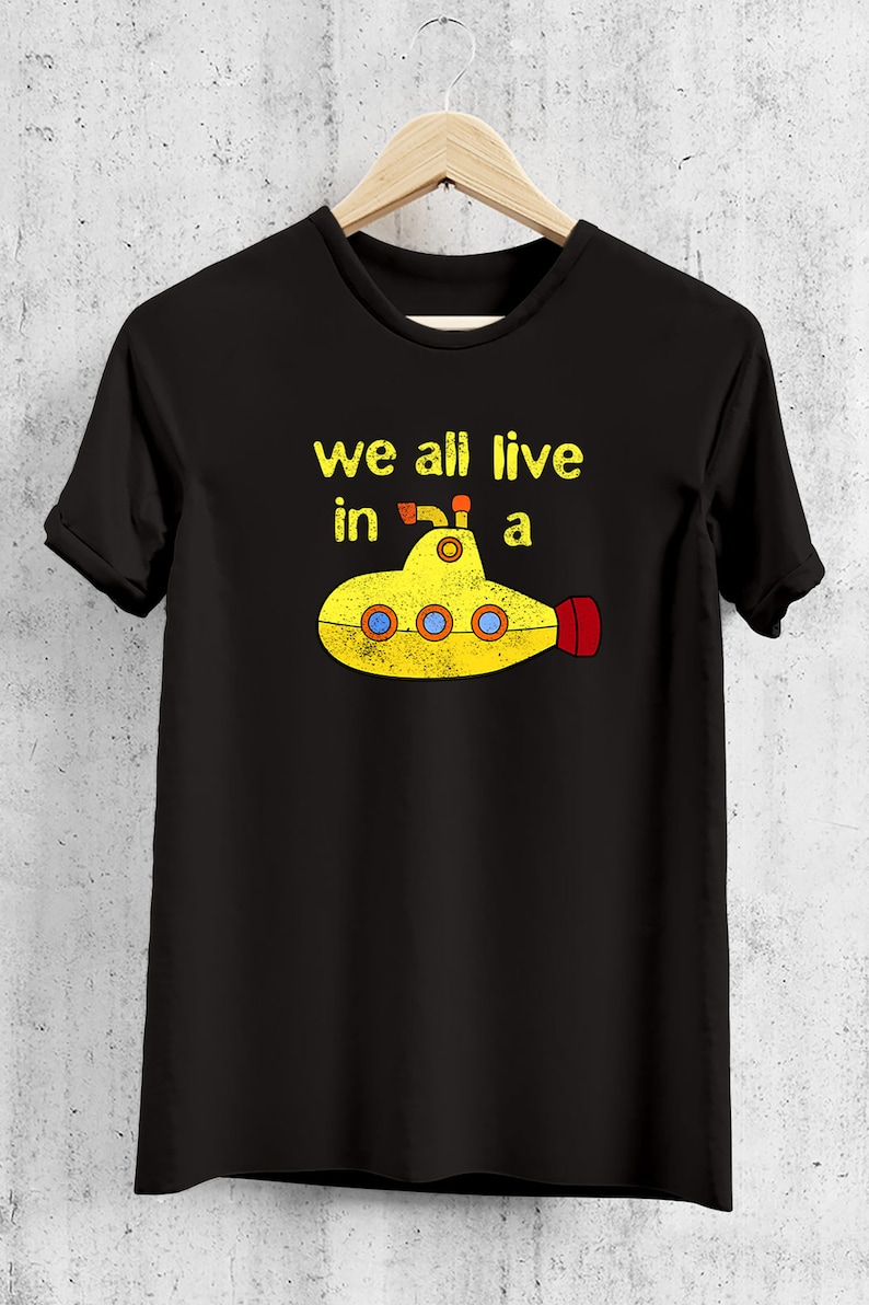 May include: Black t-shirt with a yellow submarine graphic and the text "we all live in a". The submarine has red and orange accents. The shirt is hanging on a wooden hanger.