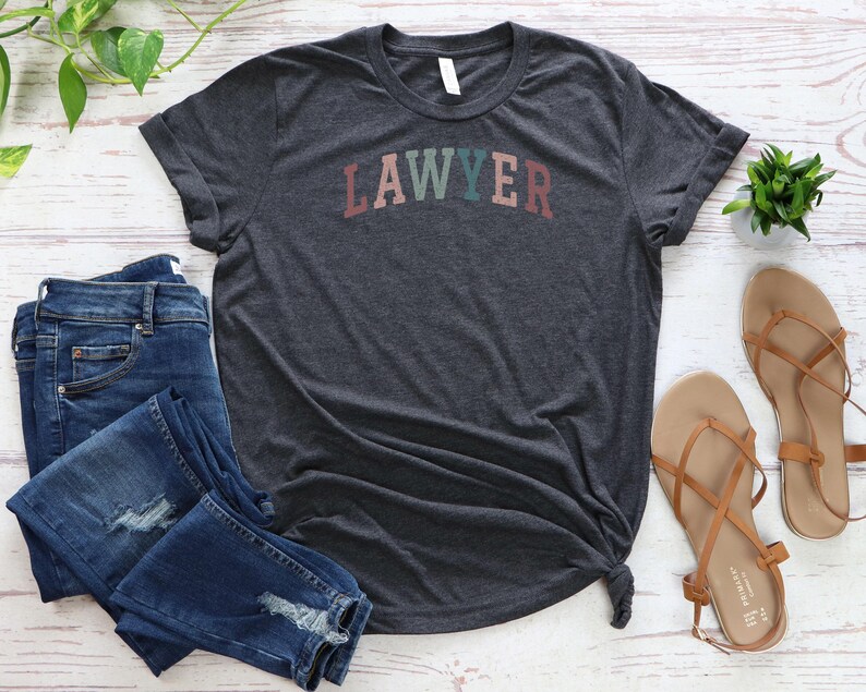 May include: A dark heather grey t-shirt with the word "LAWYER" printed in rainbow colors across the front.