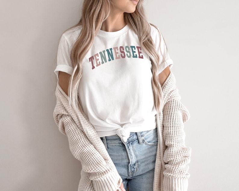 May include: A white t-shirt with the word "TENNESSEE" printed in colorful letters across the front. The letters are in shades of pink, red, green, and blue.