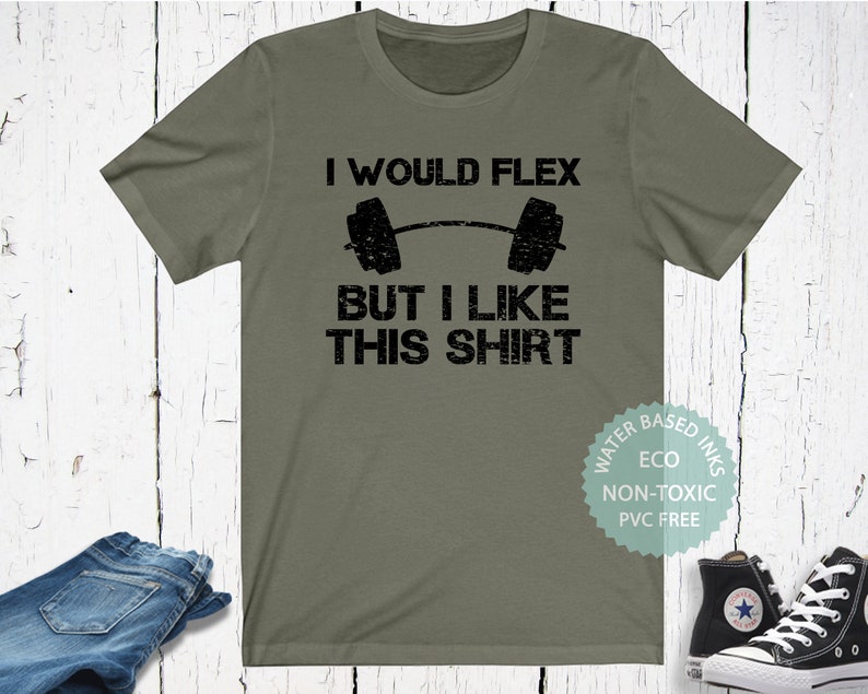 May include: A green t-shirt with the text "I would flex but I like this shirt" and a black weightlifting barbell graphic. The shirt also has a small circle with the text "Water Based Inks, Eco, Non-Toxic, PVC Free".
