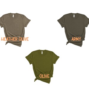 May include: Three t-shirts in different shades of green. The t-shirts are folded and laid flat on a white background. The t-shirts are labeled "Heather Olive", "Army", and "Olive".