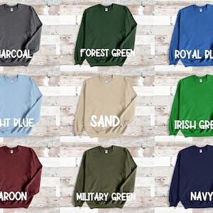 Puede incluir: Nueve sudaderas de cuello redondo de diferentes colores dispuestas sobre un fondo de madera. Los colores son carb&oacute;n, verde bosque, azul real, azul claro, arena, verde irland&eacute;s, granate, verde militar y azul marino.
