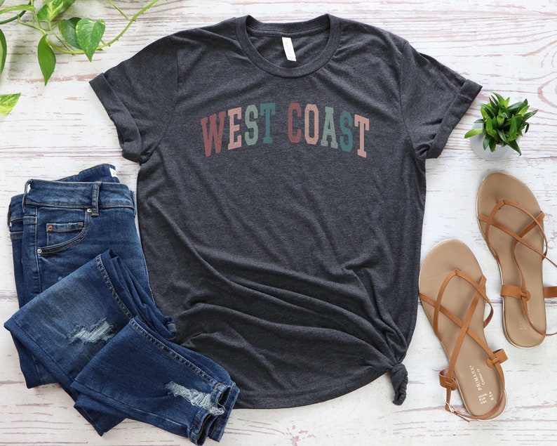May include: A dark gray t-shirt with the text "WEST COAST" in colorful letters. The letters are in shades of pink, green, blue, and orange.