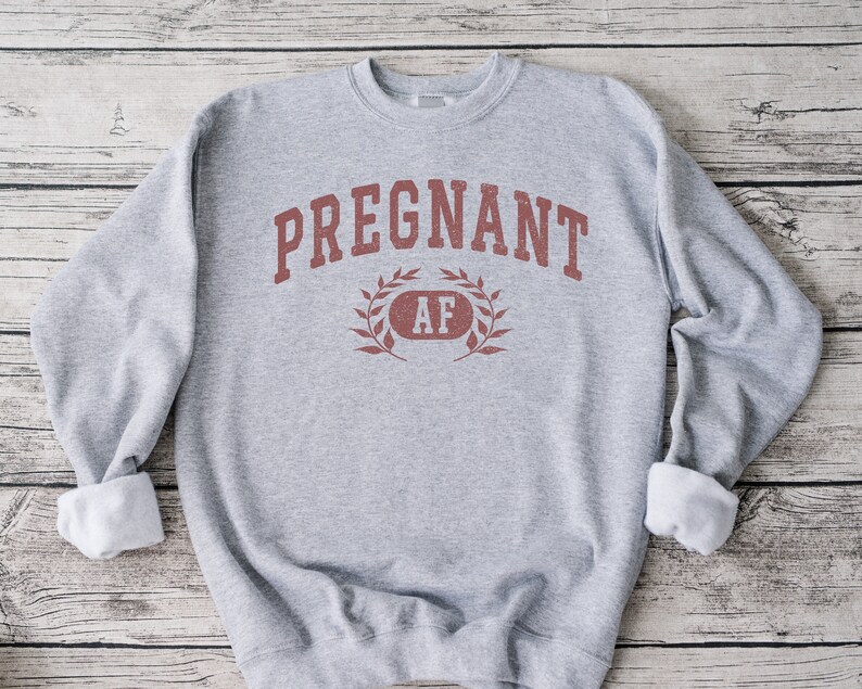 May include: Grey sweatshirt with the text "PREGNANT AF" in red lettering with a laurel wreath around the "AF".