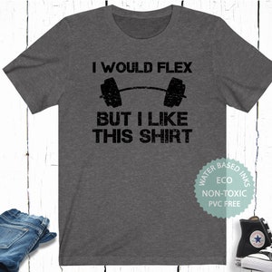 May include: A dark gray t-shirt with the text "I would flex but I like this shirt" and a black and white illustration of a barbell. The shirt is made with water-based, eco-friendly inks that are non-toxic and PVC free.