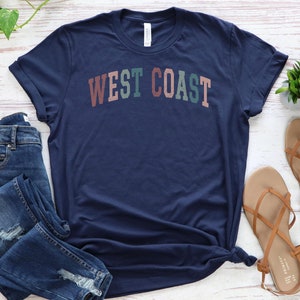 May include: A navy blue t-shirt with the text "WEST COAST" in a colorful, retro font.