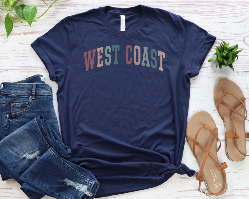 May include: A navy blue t-shirt with the text "WEST COAST" in a colorful, retro font.