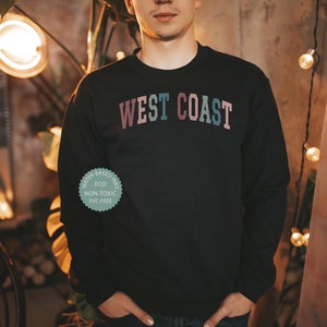 Puede incluir: Una sudadera negra con el texto "WEST COAST" impreso en un degradado arco&iacute;ris en el pecho. La sudadera est&aacute; hecha con tintas a base de agua que son ecol&oacute;gicas, no t&oacute;xicas y sin PVC.