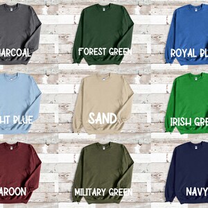 Puede incluir: Nueve sudaderas de cuello redondo de diferentes colores dispuestas sobre un fondo de madera. Los colores son carb&oacute;n, verde bosque, azul real, azul claro, arena, verde irland&eacute;s, granate, verde militar y azul marino.