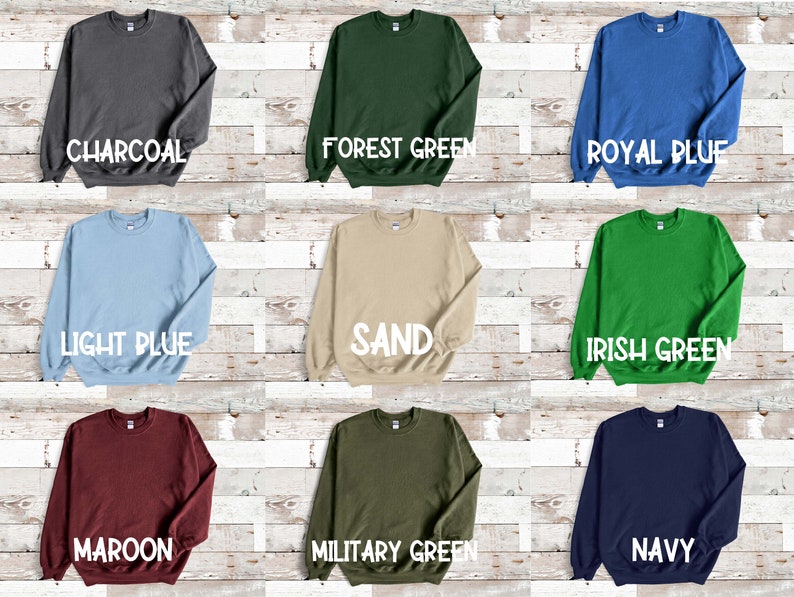 Puede incluir: Nueve sudaderas de cuello redondo de diferentes colores dispuestas sobre un fondo de madera. Los colores son carb&oacute;n, verde bosque, azul real, azul claro, arena, verde irland&eacute;s, granate, verde militar y azul marino.